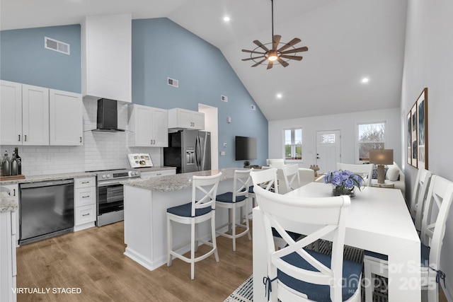 kitchen with wall chimney range hood, white cabinetry, a kitchen island, and appliances with stainless steel finishes