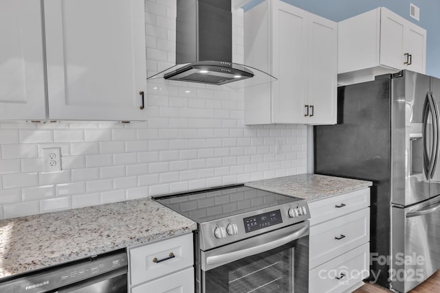 kitchen featuring decorative backsplash, appliances with stainless steel finishes, white cabinetry, light stone countertops, and wall chimney exhaust hood