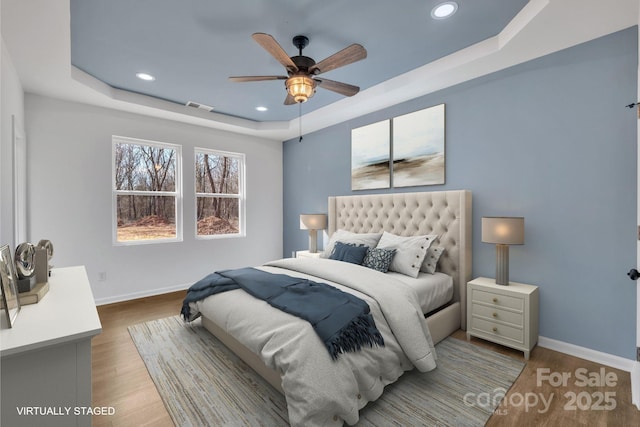 bedroom with a tray ceiling, light wood-type flooring, visible vents, and baseboards