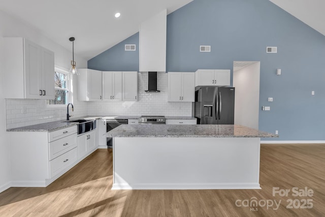 kitchen with a center island, white cabinets, a sink, black appliances, and wall chimney exhaust hood