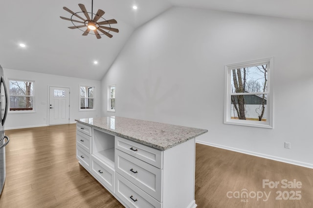 kitchen featuring a healthy amount of sunlight, light stone countertops, a kitchen island, and white cabinetry