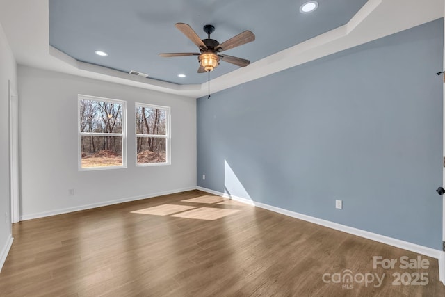 empty room with a tray ceiling, recessed lighting, visible vents, wood finished floors, and baseboards