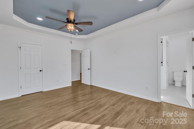 unfurnished bedroom with connected bathroom, recessed lighting, wood finished floors, baseboards, and a tray ceiling