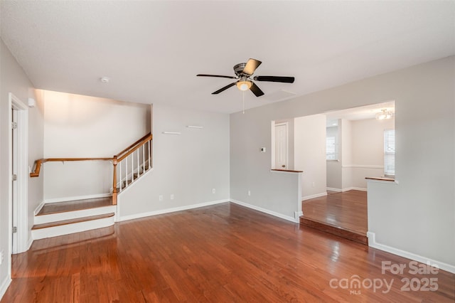 unfurnished living room with stairs, ceiling fan, wood finished floors, and baseboards