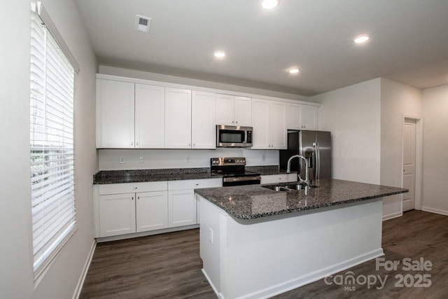 kitchen featuring stainless steel appliances, dark wood-style flooring, a sink, white cabinets, and an island with sink