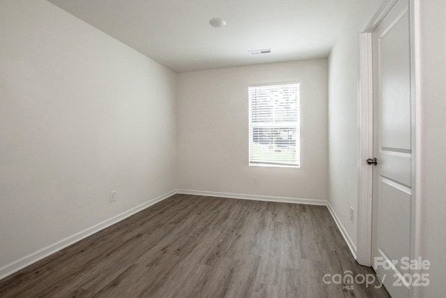 spare room with dark wood-type flooring, visible vents, and baseboards