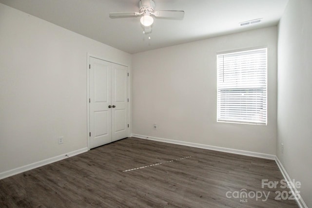 empty room with dark wood-style floors, ceiling fan, visible vents, and baseboards