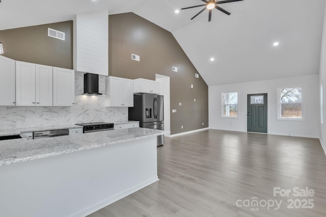 kitchen featuring stainless steel appliances, white cabinets, open floor plan, wall chimney range hood, and light stone countertops