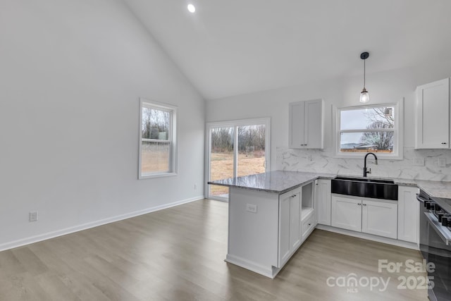 kitchen featuring hanging light fixtures, white cabinetry, a sink, light stone countertops, and a peninsula