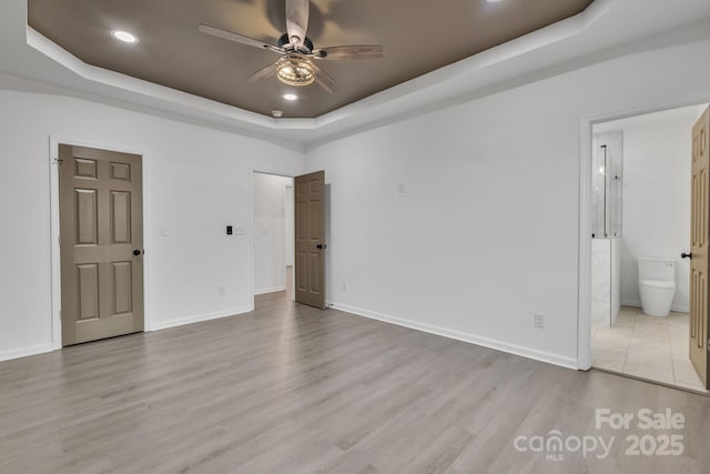 unfurnished bedroom featuring light wood finished floors, recessed lighting, a raised ceiling, connected bathroom, and baseboards