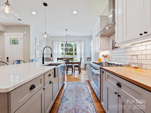 kitchen featuring wall chimney exhaust hood, hanging light fixtures, stainless steel stove, and a center island with sink