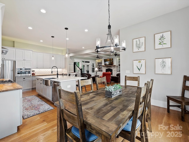 dining room with ceiling fan, a fireplace, light hardwood / wood-style floors, and sink