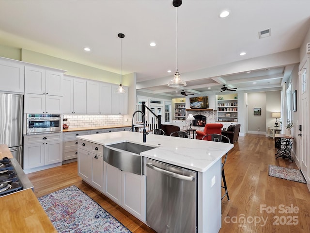 kitchen with sink, appliances with stainless steel finishes, hanging light fixtures, white cabinets, and a center island with sink