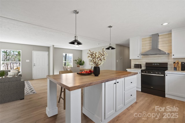 kitchen featuring white cabinetry, butcher block counters, gas stove, and wall chimney range hood