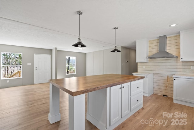 kitchen with butcher block counters, wall chimney range hood, white cabinetry, and decorative light fixtures