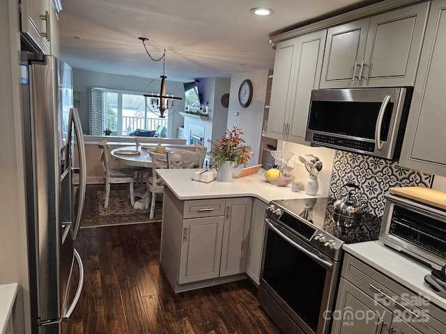 kitchen featuring pendant lighting, gray cabinets, appliances with stainless steel finishes, dark hardwood / wood-style flooring, and kitchen peninsula