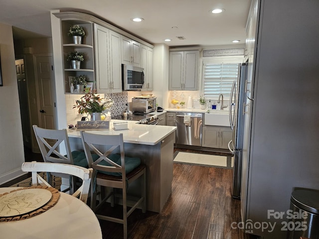 kitchen with sink, tasteful backsplash, dark hardwood / wood-style floors, kitchen peninsula, and stainless steel appliances