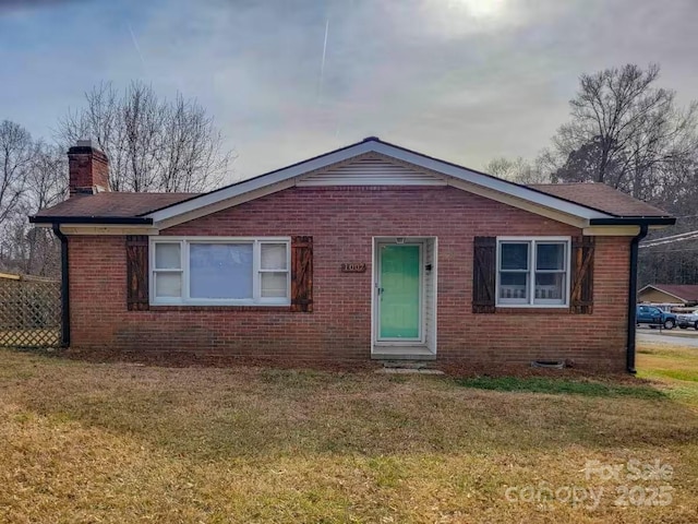 view of front facade with a front yard, brick siding, and a chimney