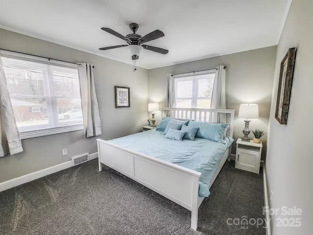 bedroom with baseboards, visible vents, a ceiling fan, dark colored carpet, and crown molding