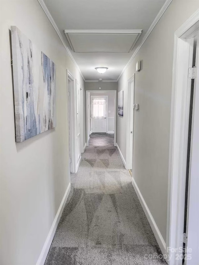 hallway with baseboards, ornamental molding, attic access, and light colored carpet