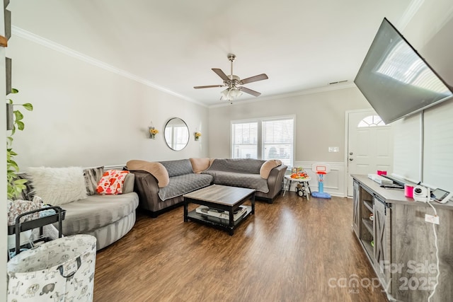 living area featuring ornamental molding, dark wood-style flooring, a wainscoted wall, and a ceiling fan