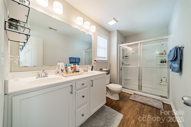 bathroom featuring double vanity, visible vents, wood finished floors, a shower stall, and a sink