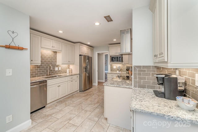 kitchen featuring stainless steel appliances, visible vents, island range hood, light stone countertops, and a sink