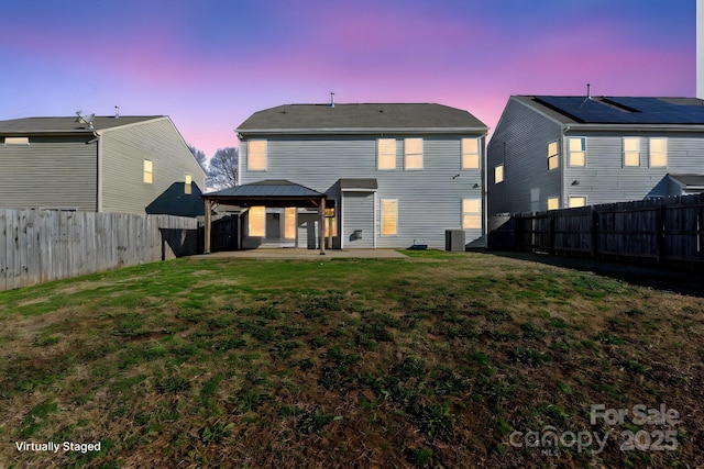 back house at dusk with central air condition unit, a patio, a lawn, and a gazebo