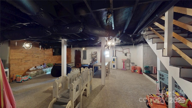 unfinished below grade area featuring stairs, carpet floors, wooden walls, and water heater