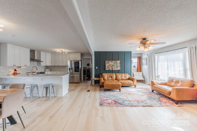 living area with light wood-style flooring, a textured ceiling, and a ceiling fan