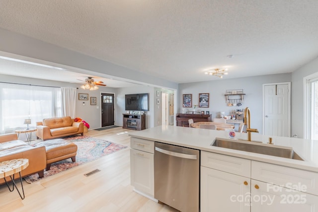 kitchen with open floor plan, dishwasher, a textured ceiling, white cabinetry, and a sink