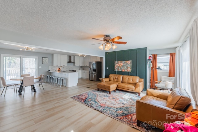 living room featuring ceiling fan with notable chandelier, light wood-type flooring, and a textured ceiling