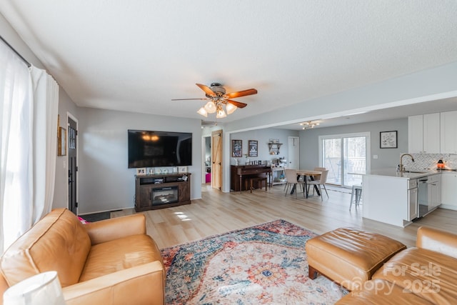 living room with light wood finished floors, a glass covered fireplace, and a ceiling fan