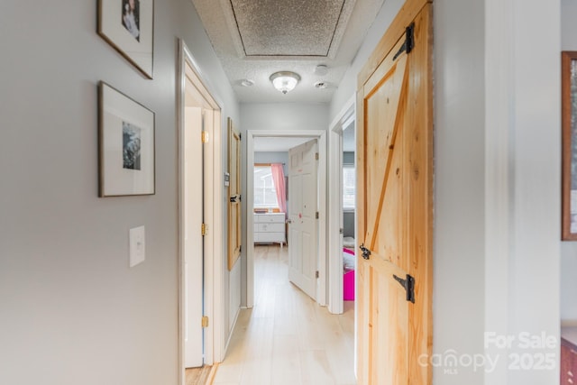 corridor with light wood-style floors and a textured ceiling