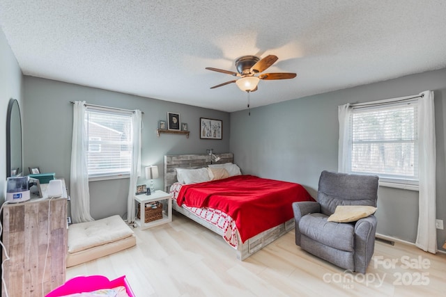 bedroom featuring ceiling fan, wood finished floors, visible vents, and a textured ceiling