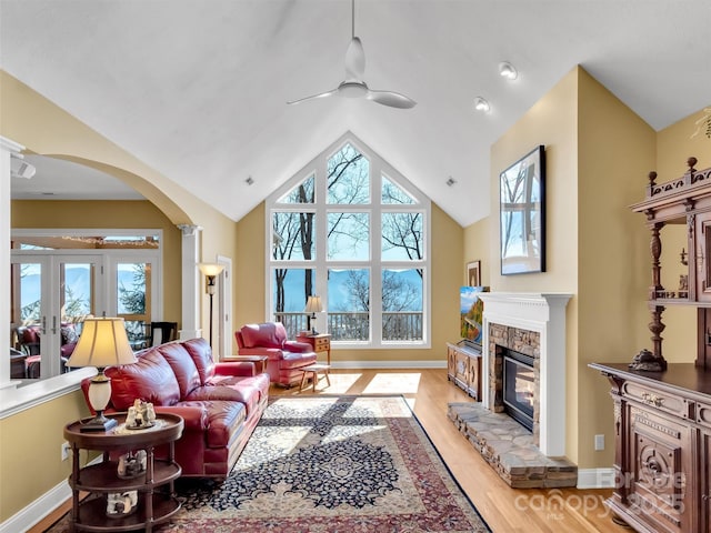 living room with baseboards, arched walkways, ceiling fan, wood finished floors, and a stone fireplace