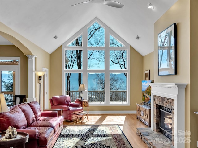 living room featuring ornate columns, light wood-style flooring, a fireplace, and visible vents