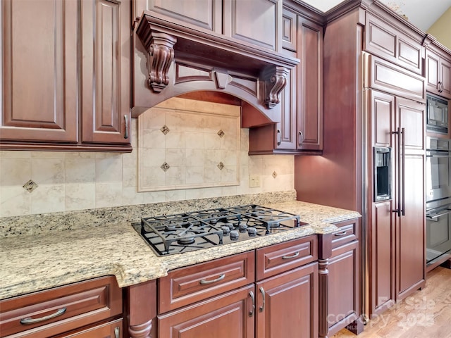 kitchen featuring light stone counters, light wood-style floors, custom exhaust hood, black appliances, and tasteful backsplash