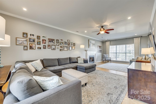 living room with a fireplace, ornamental molding, ceiling fan, and light hardwood / wood-style flooring