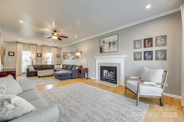 living room featuring light wood-type flooring, a tile fireplace, crown molding, and ceiling fan