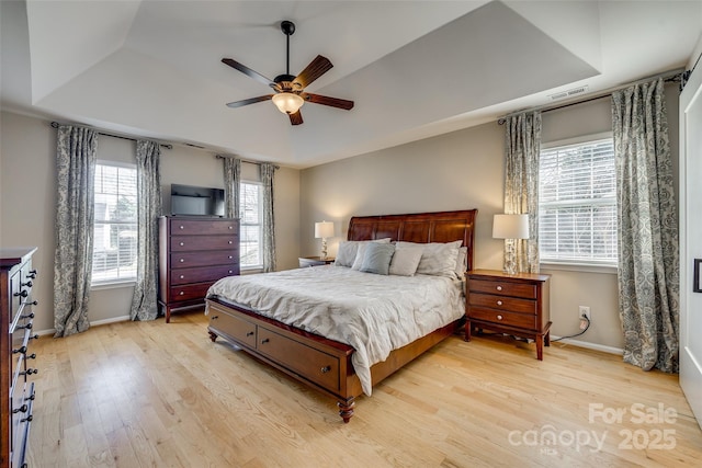 bedroom with light hardwood / wood-style flooring, ceiling fan, and a raised ceiling