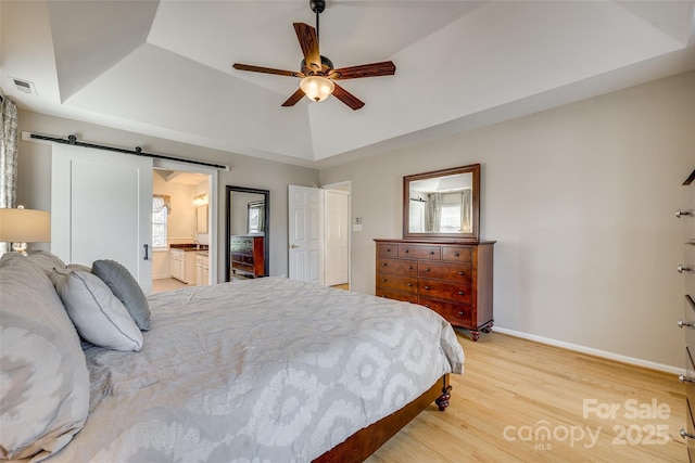 bedroom featuring ceiling fan, light hardwood / wood-style flooring, a tray ceiling, and a barn door