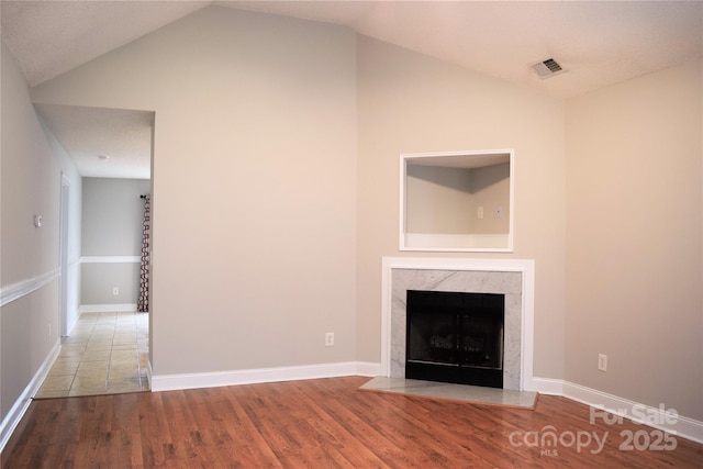 unfurnished living room featuring wood finished floors, a high end fireplace, visible vents, vaulted ceiling, and baseboards