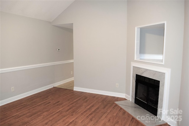 unfurnished living room featuring a fireplace with flush hearth, baseboards, vaulted ceiling, and wood finished floors