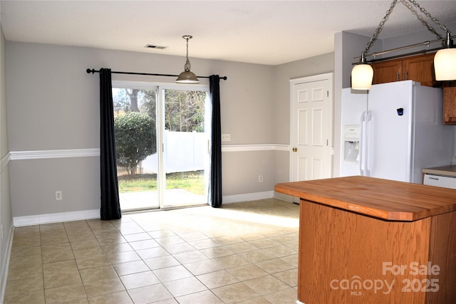 kitchen featuring white refrigerator with ice dispenser, hanging light fixtures, wood counters, and light tile patterned floors