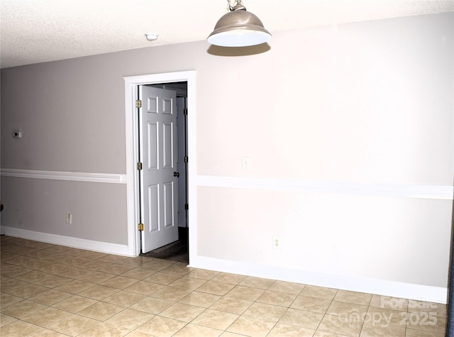 empty room with light tile patterned flooring, a textured ceiling, and baseboards