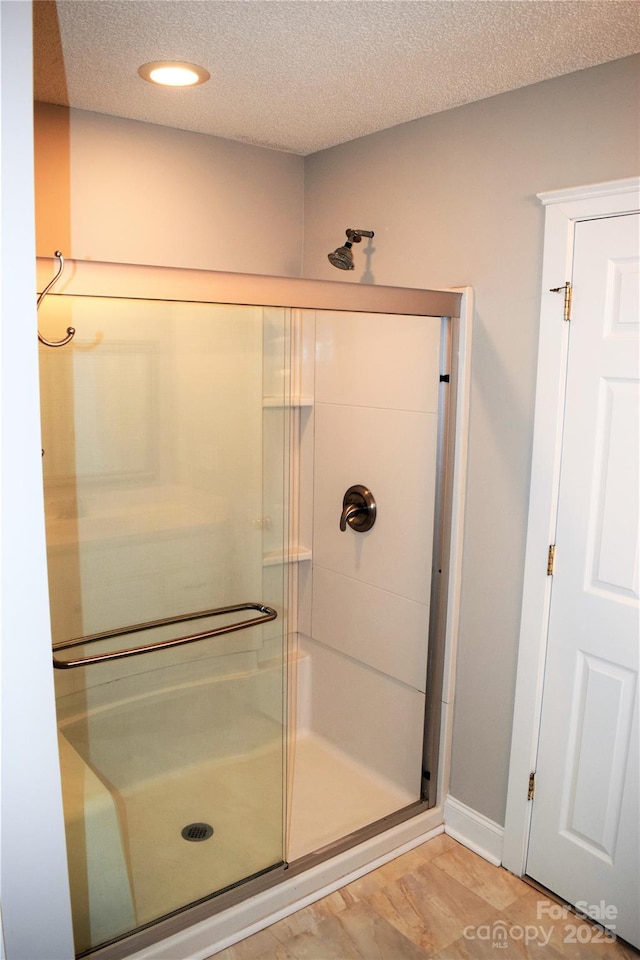 full bath with a stall shower, baseboards, and a textured ceiling