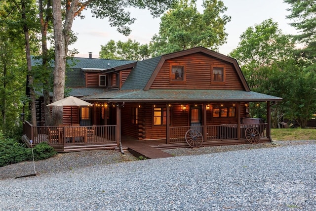 log cabin with covered porch, a shingled roof, log siding, and a gambrel roof