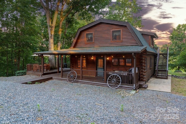 view of front facade featuring a porch, roof with shingles, log exterior, and a gambrel roof