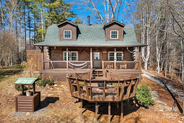 view of front facade with a shingled roof, log exterior, and a wooden deck